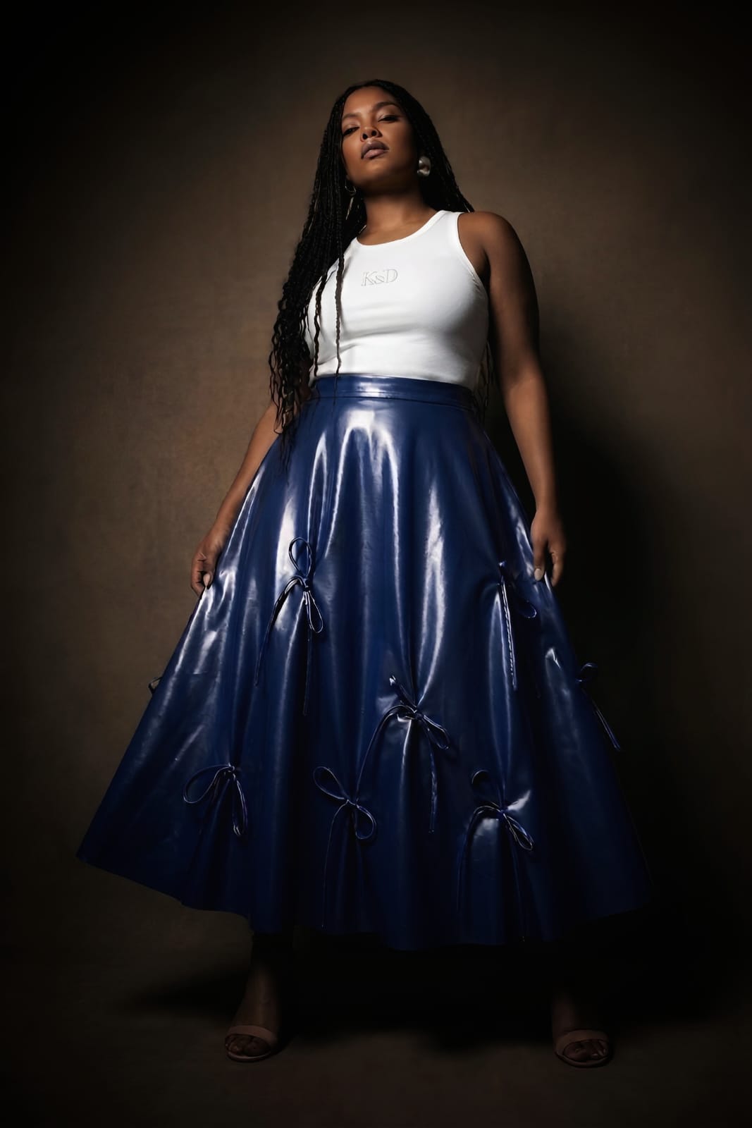 
plus size Woman wearing a white top and blue kingdom of daughters skirt against a dark background