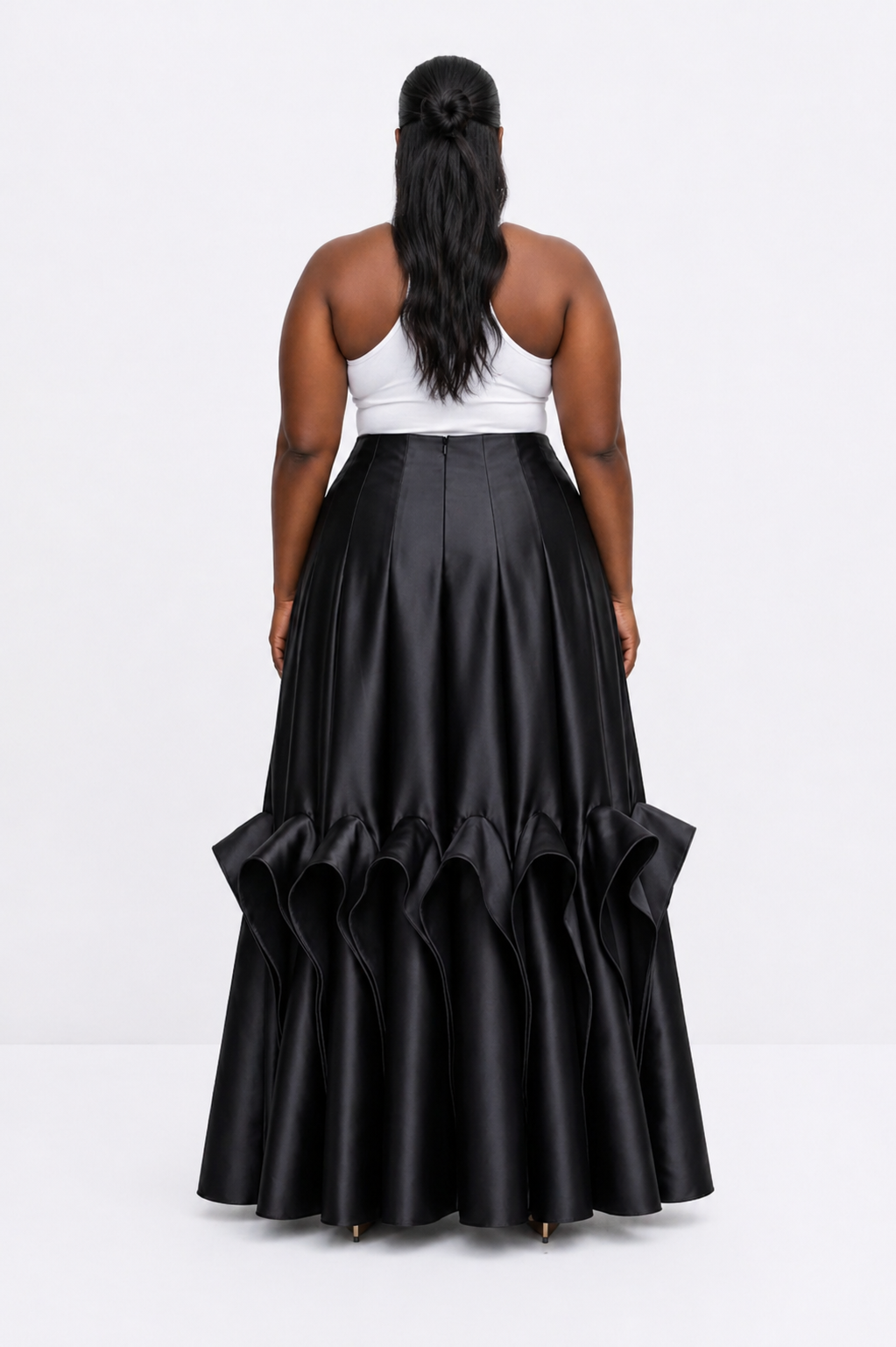Person wearing a long black ruffled skirt with a white top on a light gray background