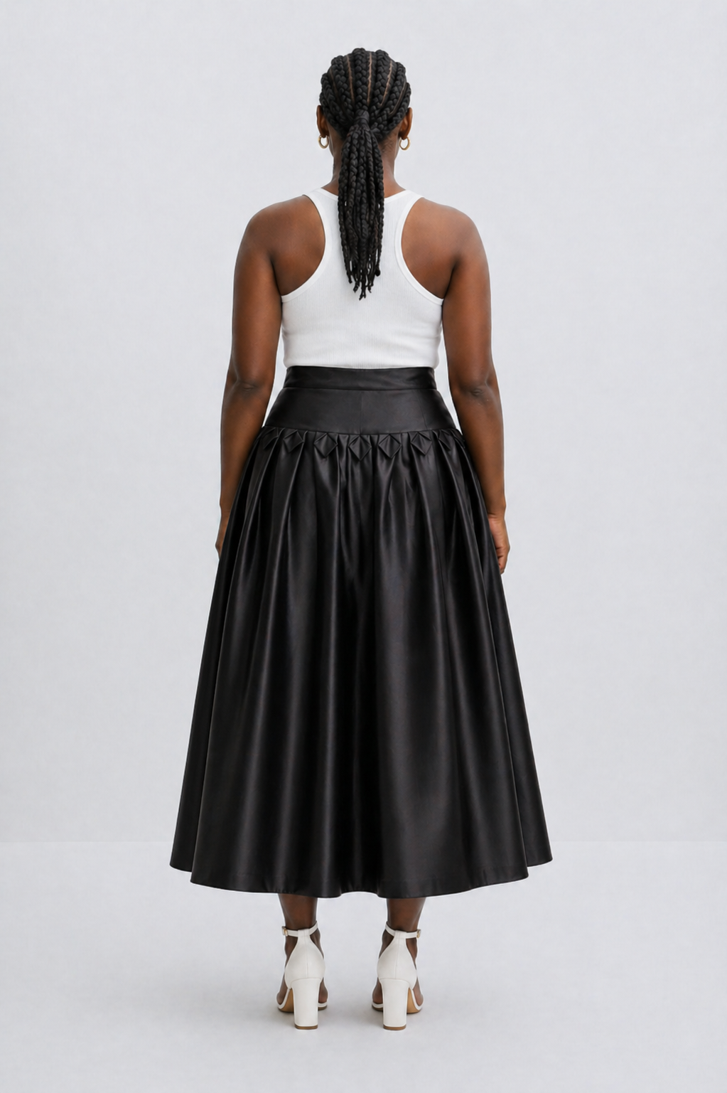 Person wearing a black leather skirt and white top on a light gray background