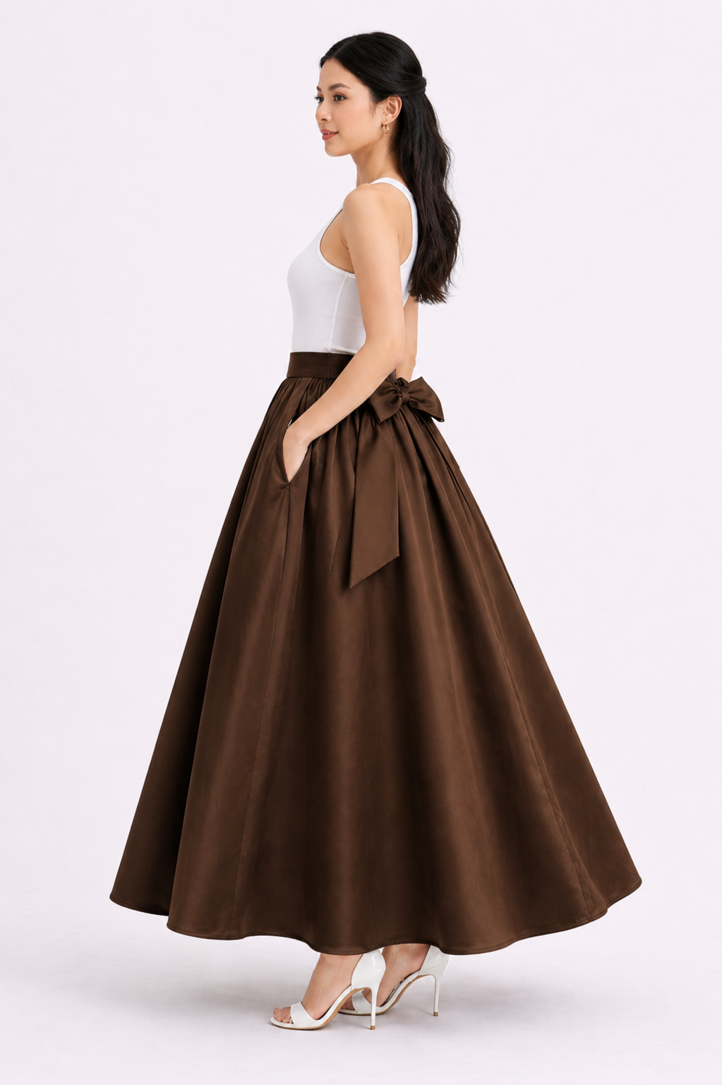 Woman wearing a brown full skirt with a white top on a light pink background