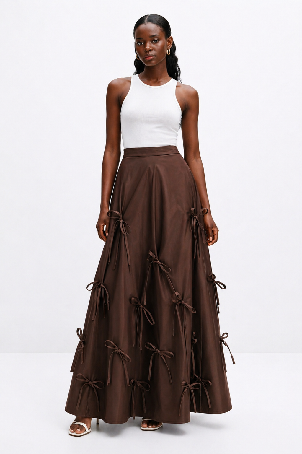 Woman wearing a white top and brown long skirt with bow details on a white background
