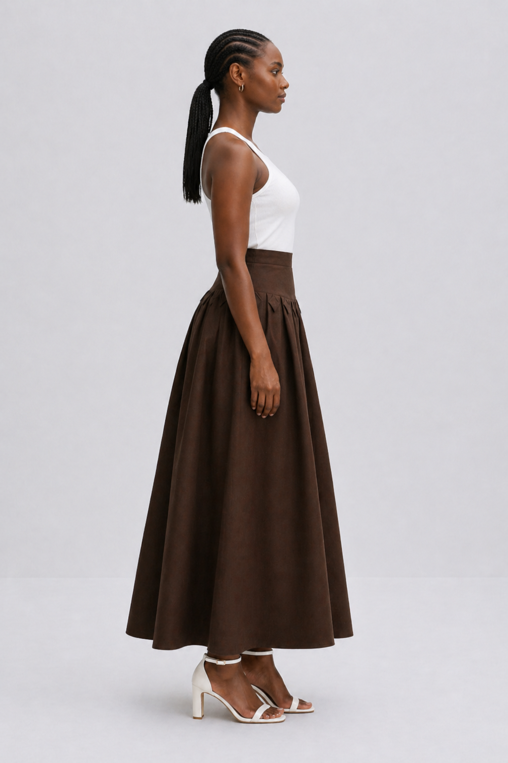 Woman wearing a white top and brown skirt on a gray background