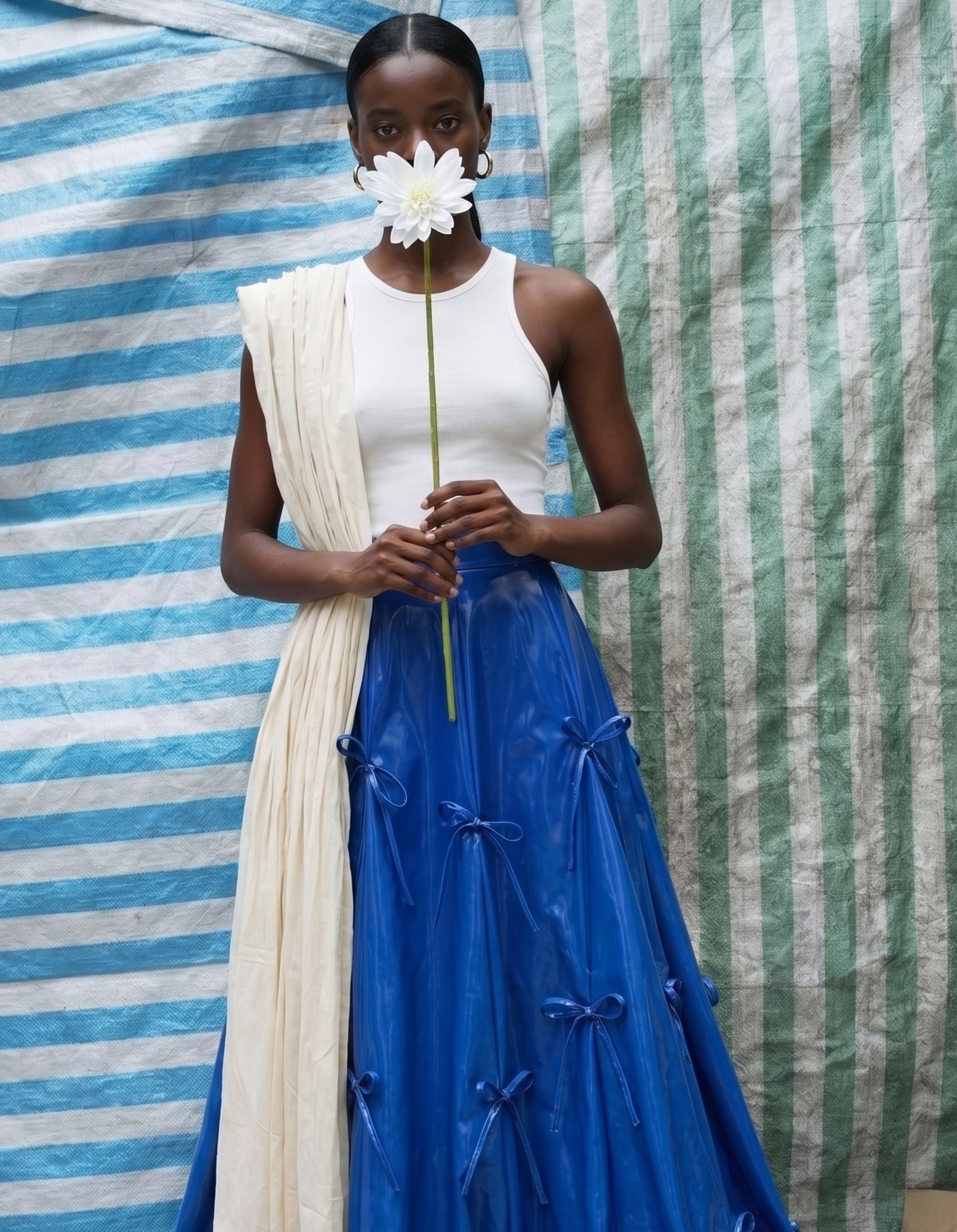 Woman wearing a blue kingdom of daughters skirt holding a white flower in front of her face against a striped fabric background