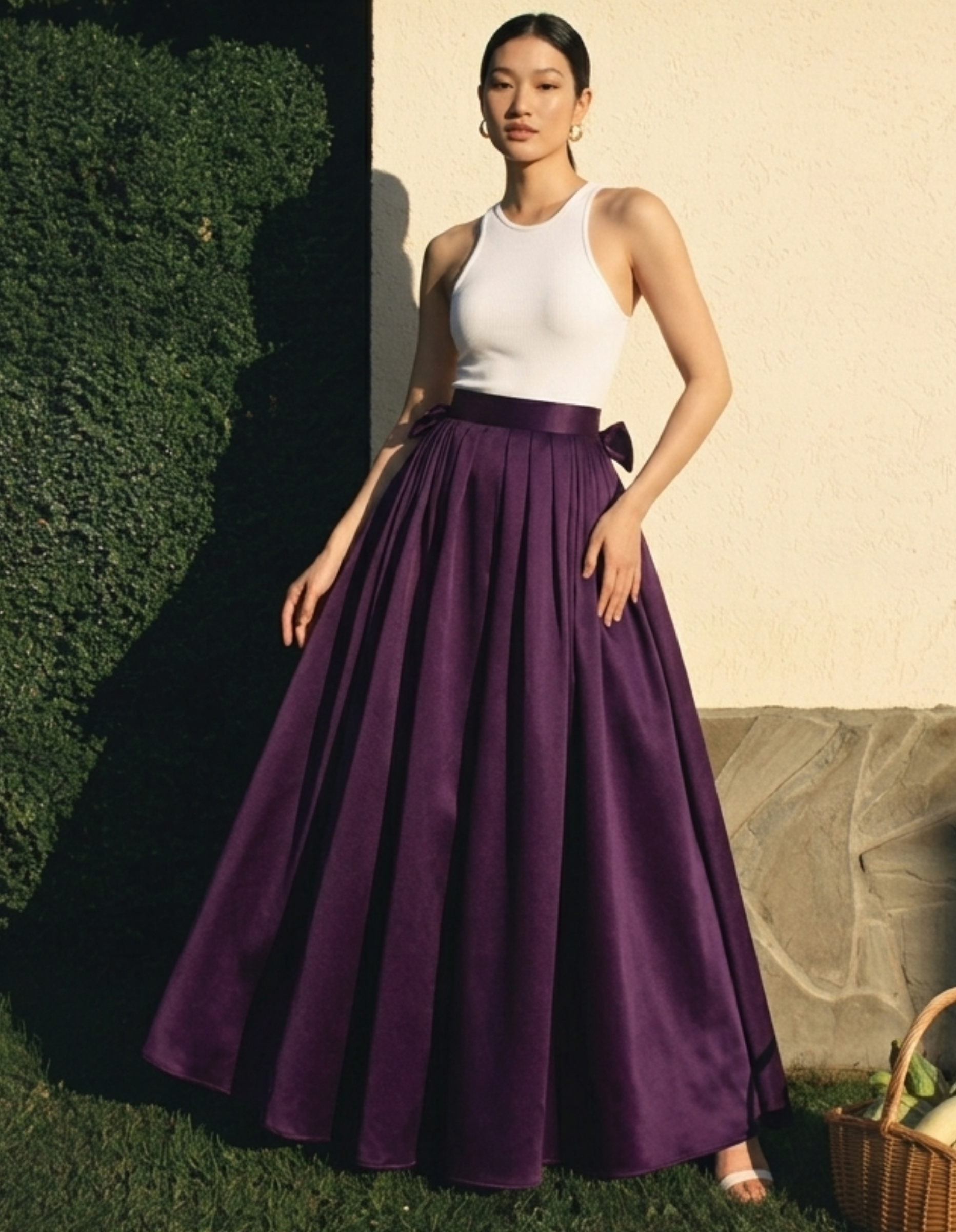 Woman wearing a white top and purple skirt standing outdoors.