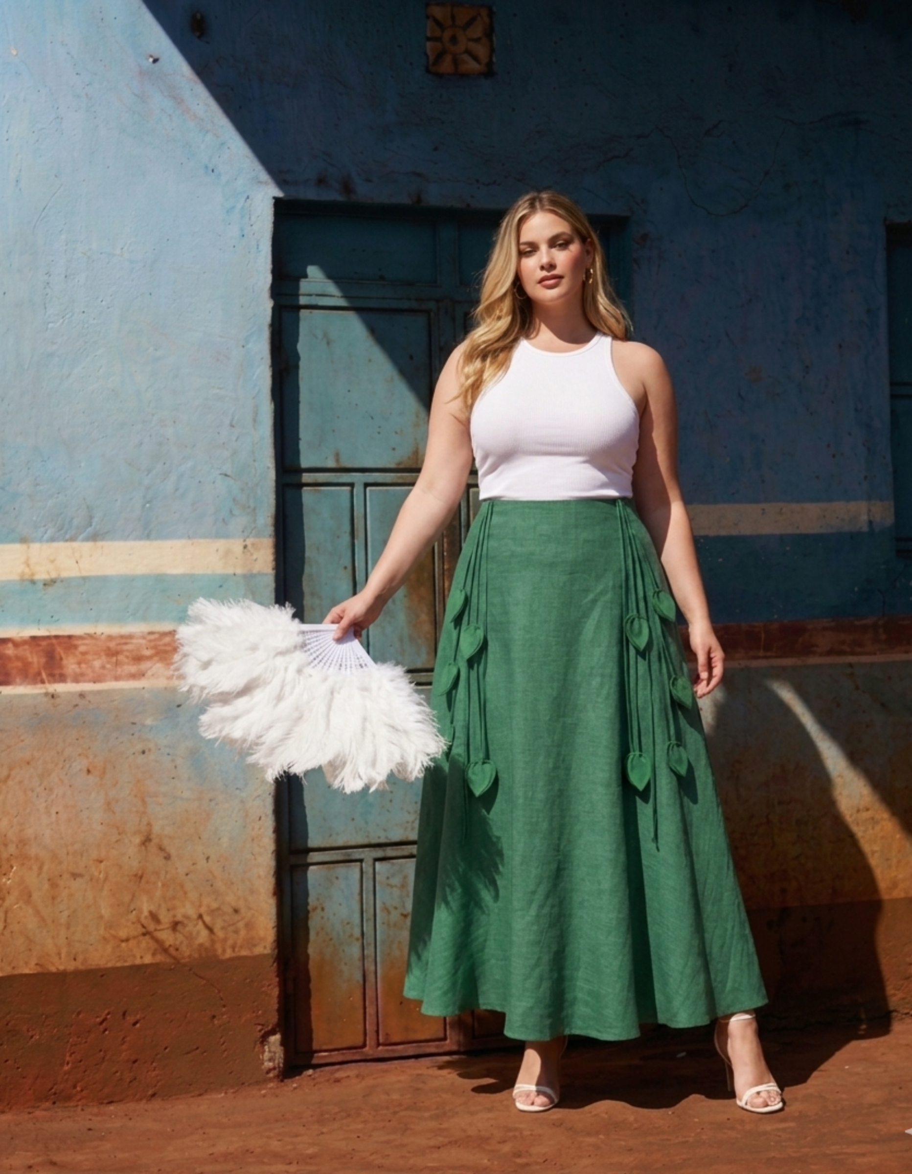 Woman in a white top and green skirt standing in front of a blue wall.