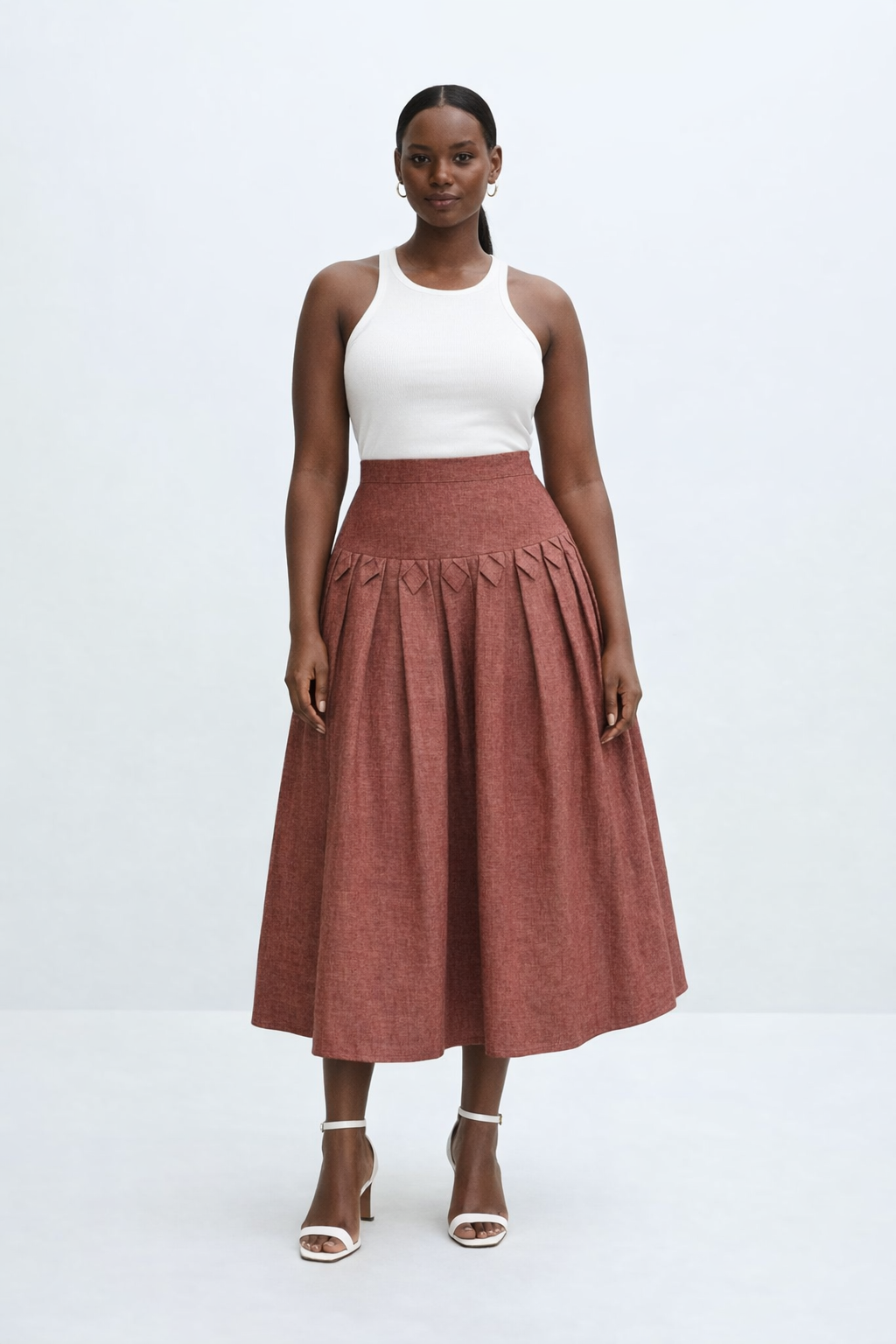Woman wearing a white top and rust-colored kingdom of daughters skirt on a white background
