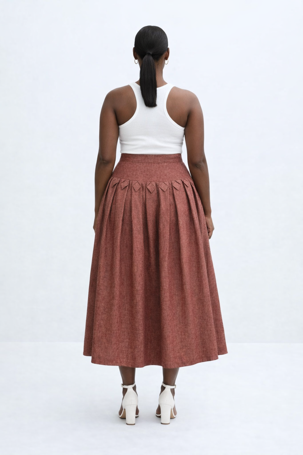 Woman wearing a white top and rust-colored kingdom of daughters skirt on a white background