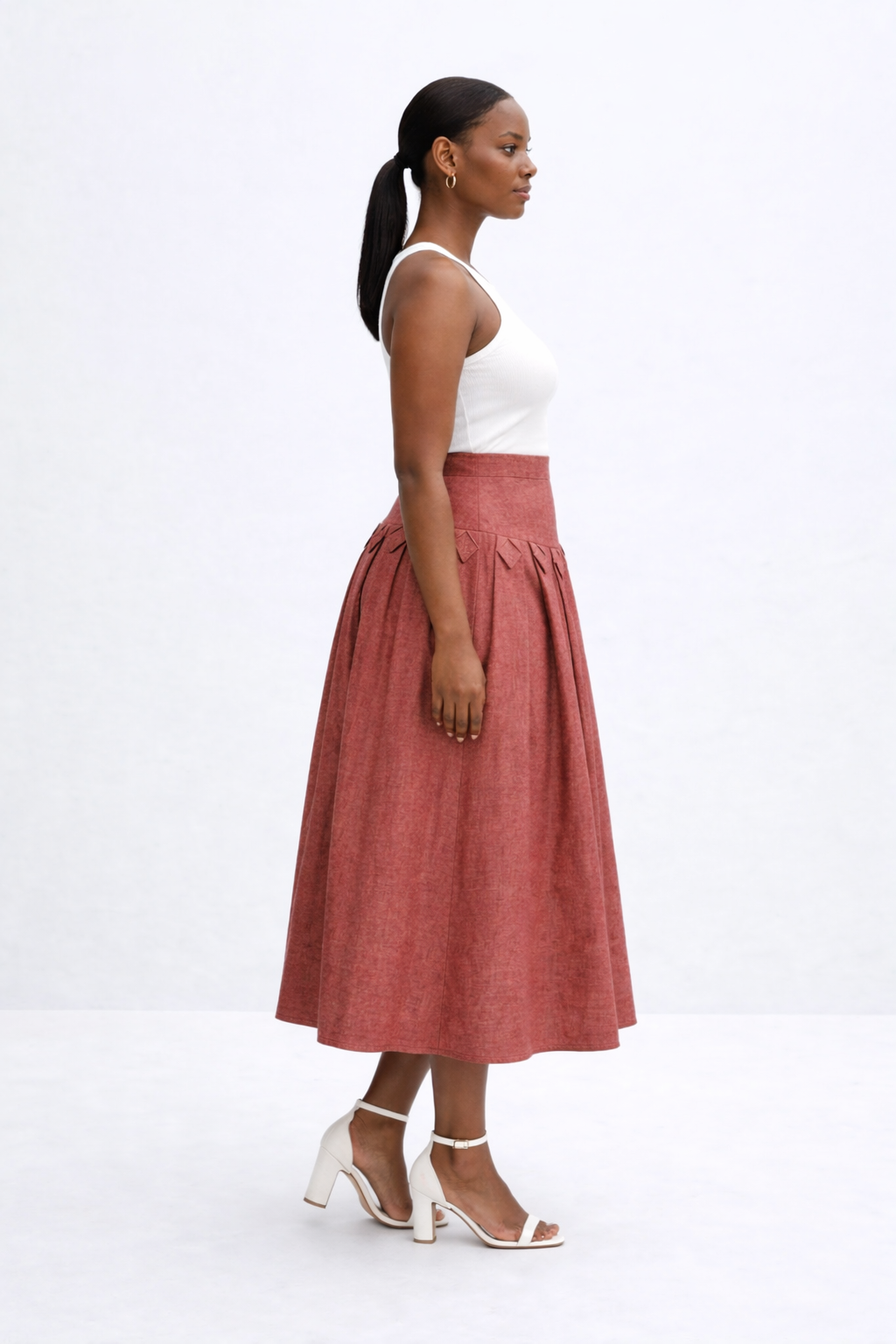 Woman wearing a white top and rust-colored kingdom of daughters skirt on a white background